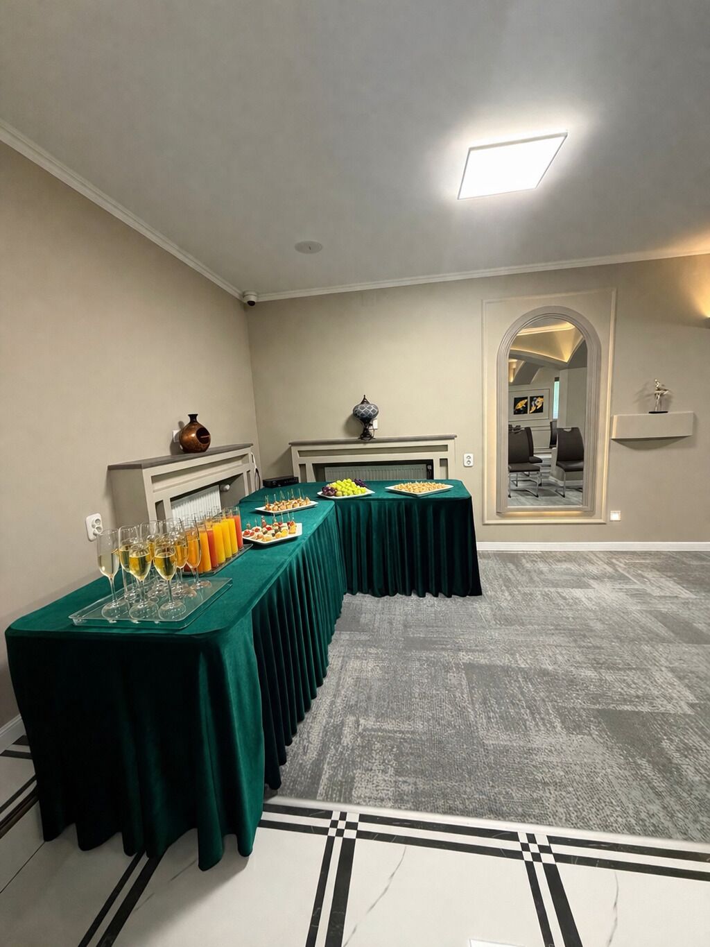 Un salón de conferencias con una larga mesa cubierta con un mantel verde, copas de vino y fuentes de fruta.
