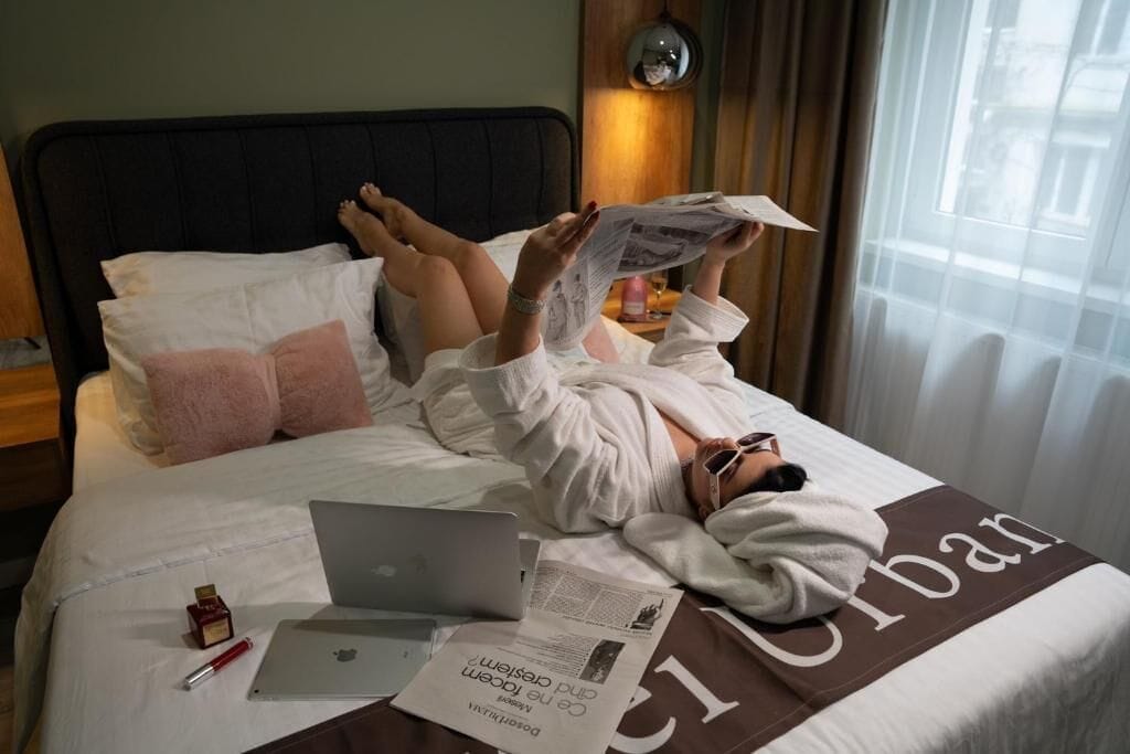 A bed with a laptop, a newspaper, and a bottle of lotion.