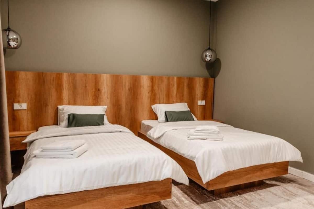 Habitación de hotel con dos camas individuales, cabeceros de madera y una decoración en tonos neutros.