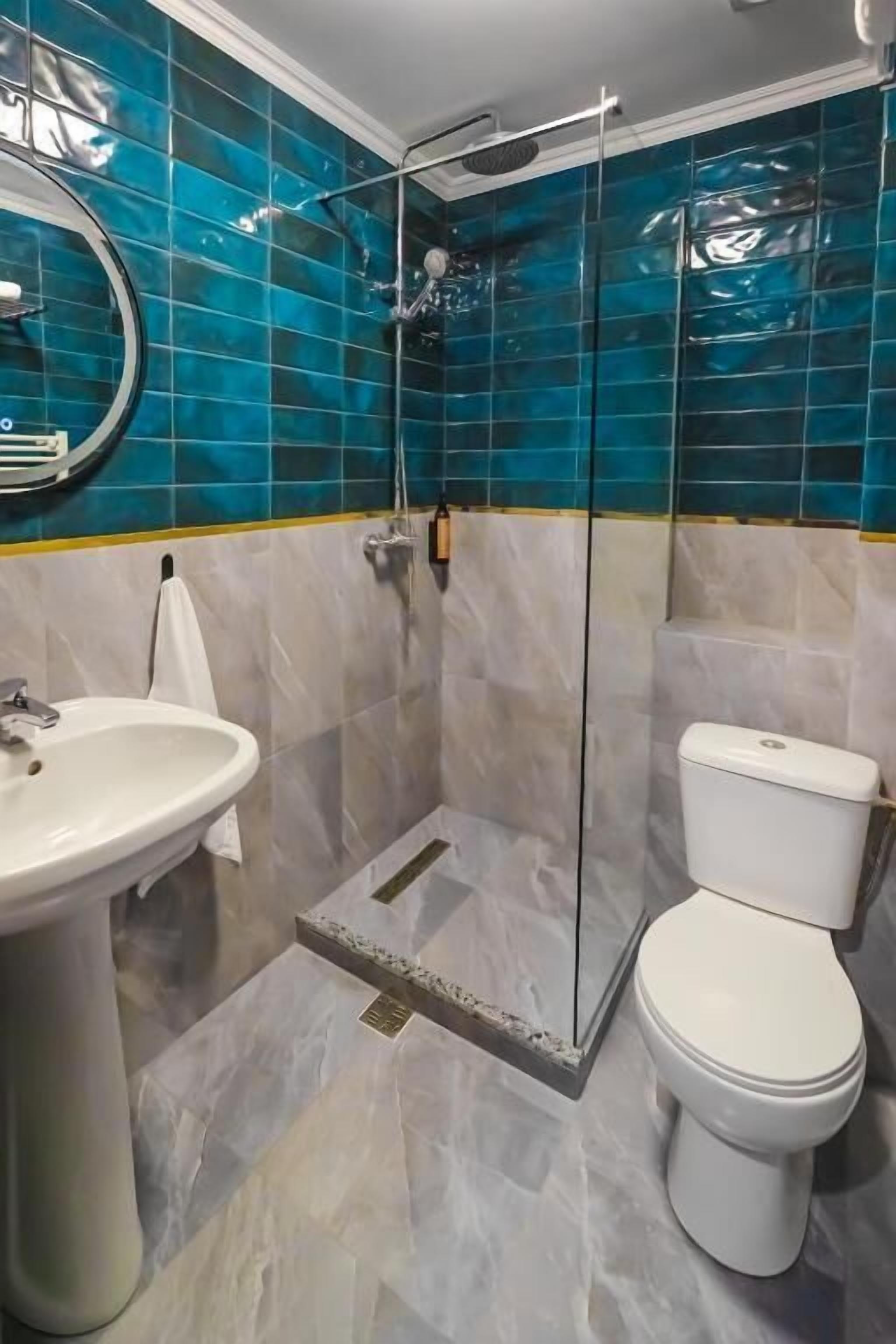 Un baño con ducha de vidrio, lavamanos blanco y retrete.