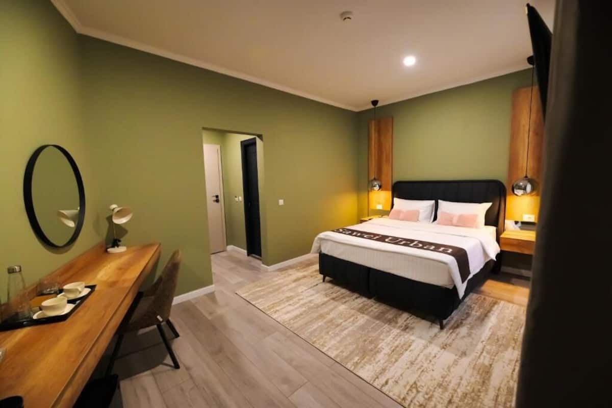 Un dormitorio con cama, lámparas de noche, un escritorio con silla y un espejo.