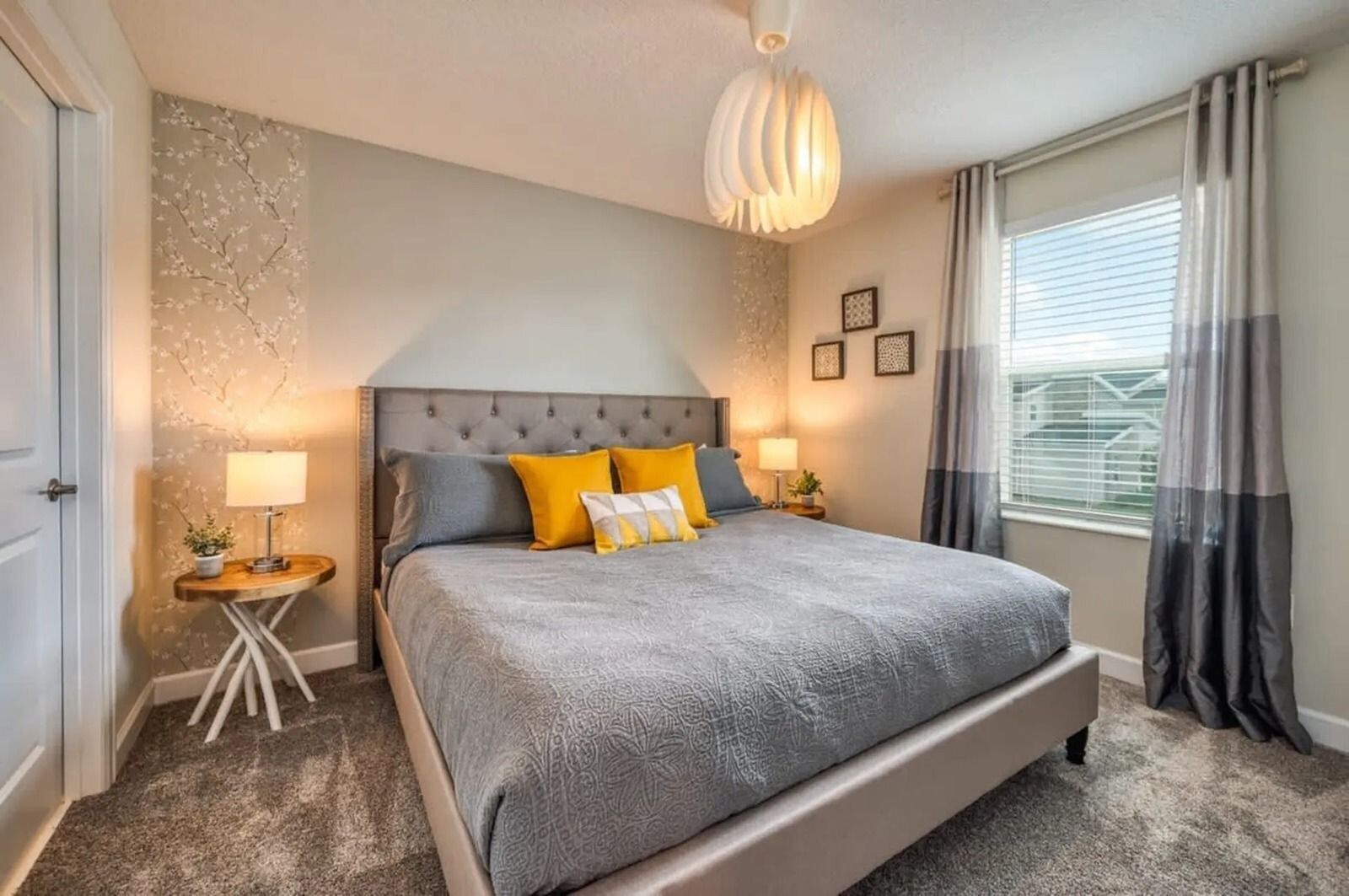 A bedroom with a large bed, two bedside tables, a hanging light fixture, and a window with curtains.