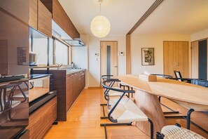 Cozinha moderna com armários de madeira, uma ilha grande e uma área de jantar com uma mesa comprida e cadeiras.