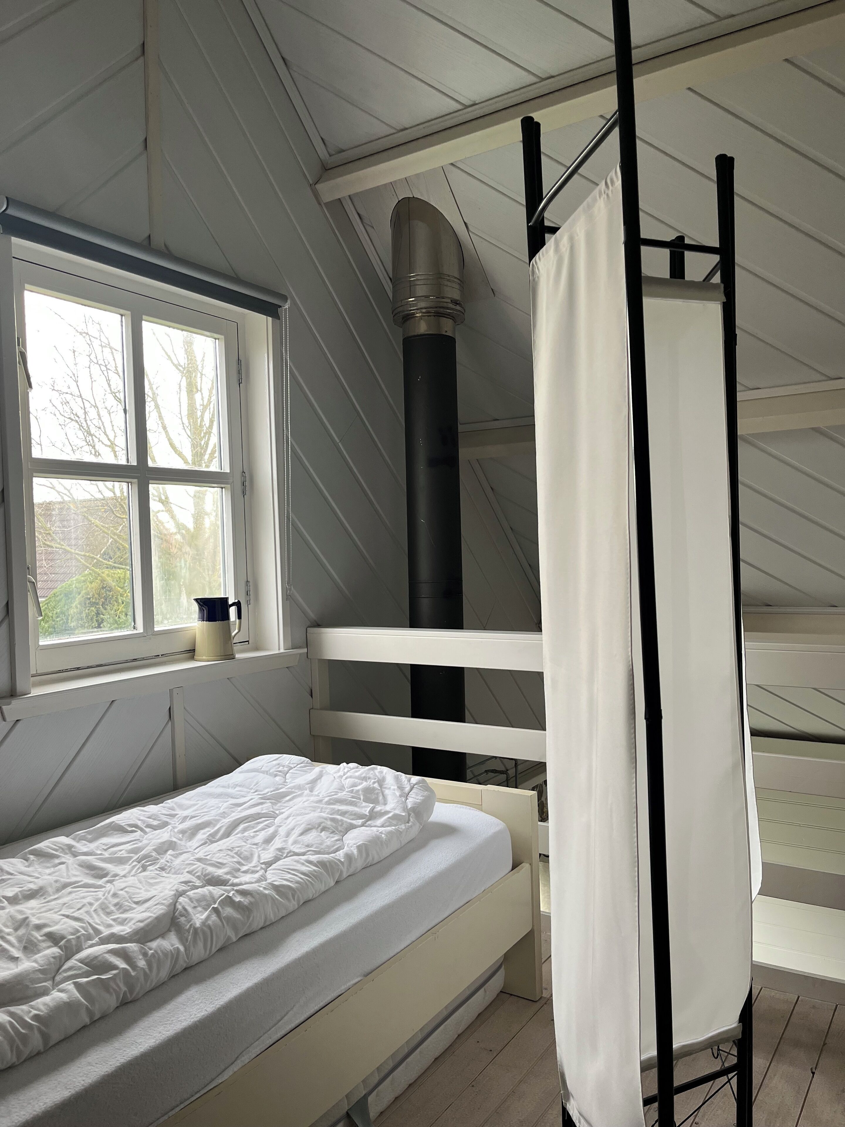 A bedroom with a bunk bed, a window, a heater, and a curtain.