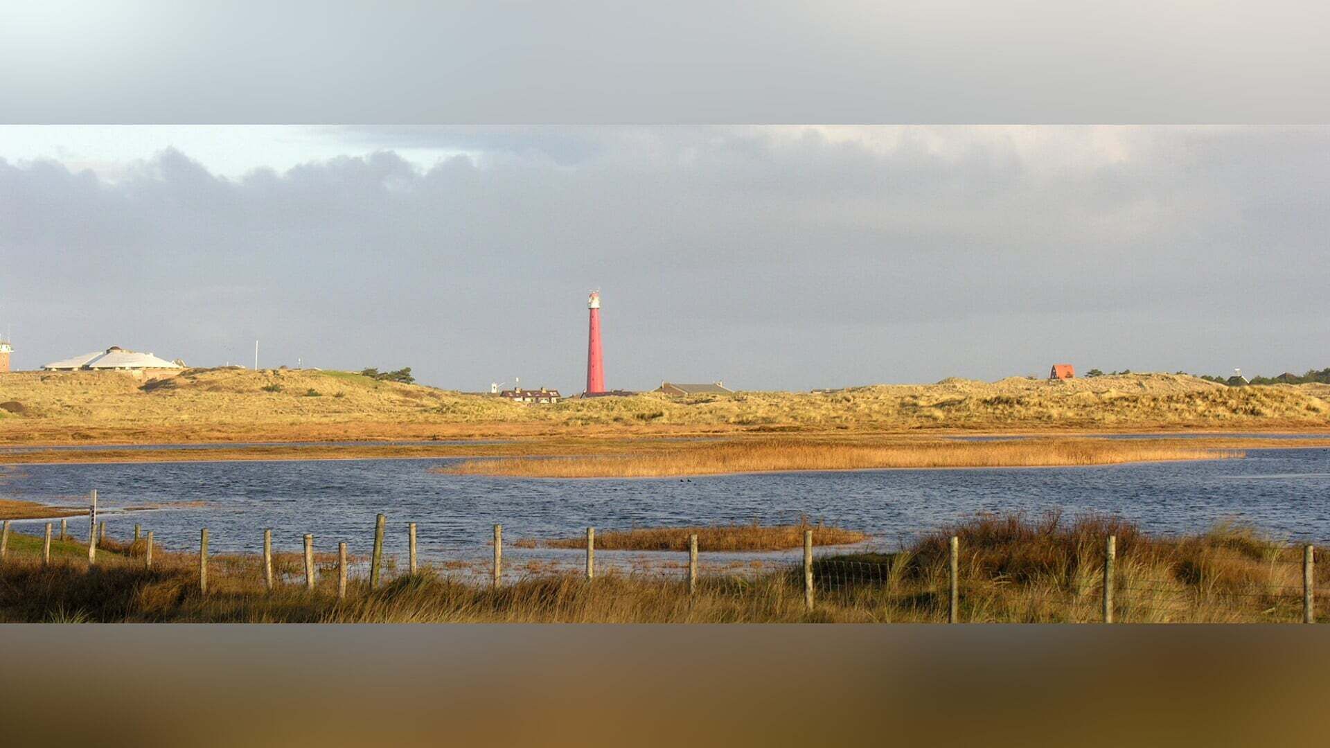 A coastal landscape with a prominent red lighthouse, a sandy beach, and a body of water.