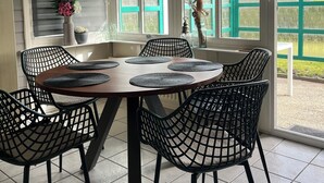 A dining area with a round table, black wire mesh chairs, and a hanging light fixture. - For rent Island Happiness! (Oudesluis)
