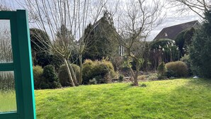 A green lawn with a wooden fence, a variety of trees and shrubs, and a house in the background. - For rent Island Happiness! (Oudesluis)