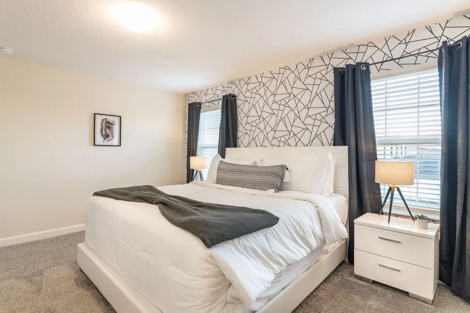 Un dormitorio moderno con una cama grande, una mesita de noche con lámpara y una pared con estampado geométrico.