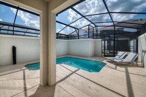 An outdoor swimming pool with a glass enclosure, lounge chairs, and a clear view of the sky. - 4-bedroom Home With Private Pool Near Disney (Kissimmee)