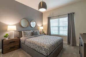 A bedroom with a bed, two bedside tables with lamps, a mirror, a window with curtains, and a small plant on the left side. - 4-bedroom Home With Private Pool Near Disney (Kissimmee)