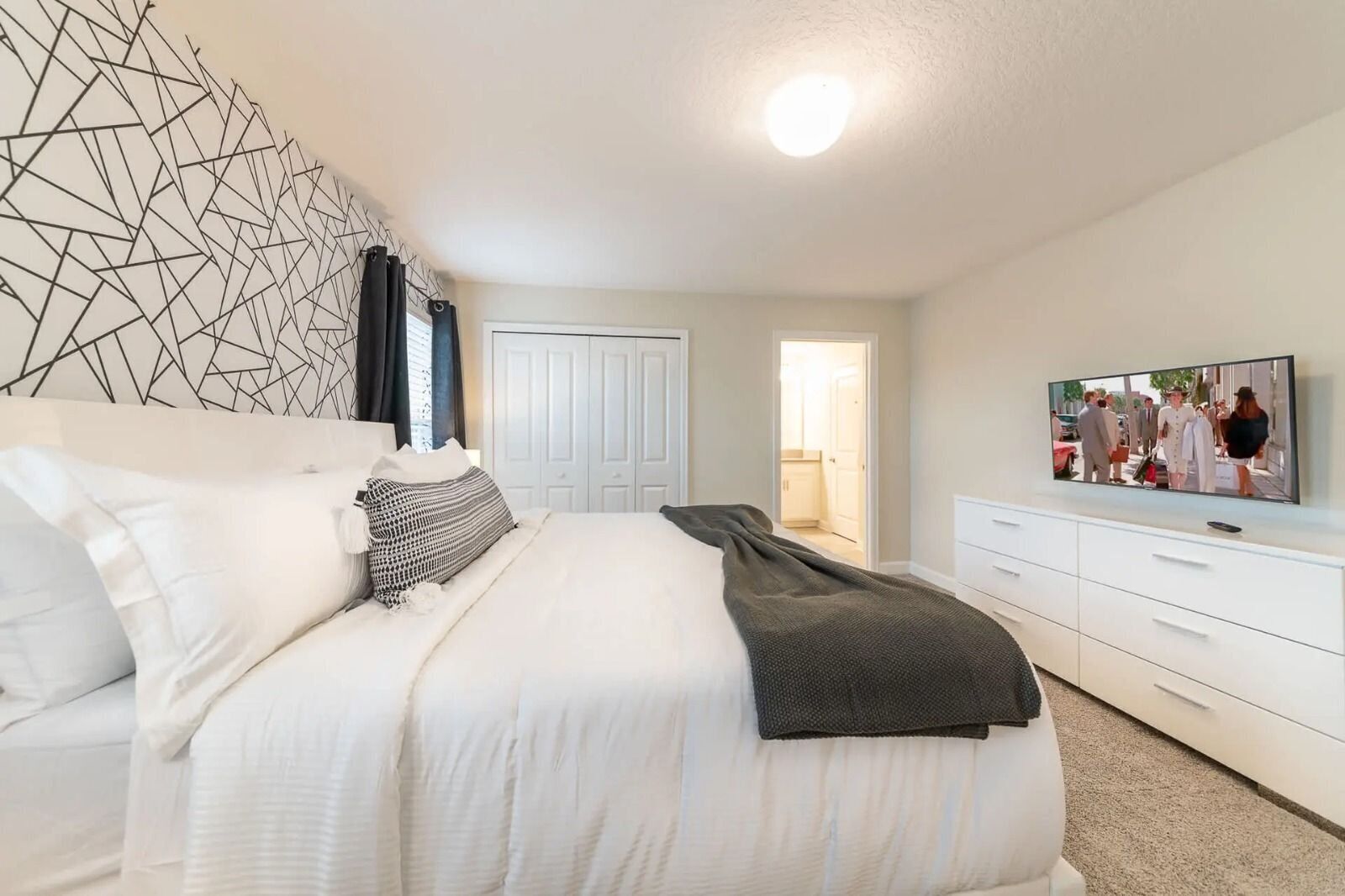 A modern bedroom with a large bed, a TV mounted on the wall, and a walk-in closet.