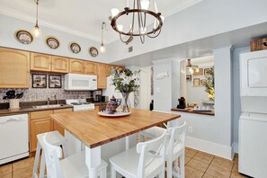 A modern kitchen with wooden cabinets, a central island, white chairs, and a chandelier. - Charming Downtown Apartment (Savannah)