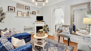 A living room with a fireplace, blue furniture, a television, and wall-mounted decorations. - Charming Downtown Apartment (Savannah)