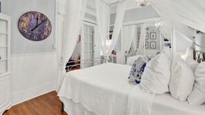 A bedroom with a bed, white curtains, a clock, and a chandelier. - Charming Downtown Apartment (Savannah)