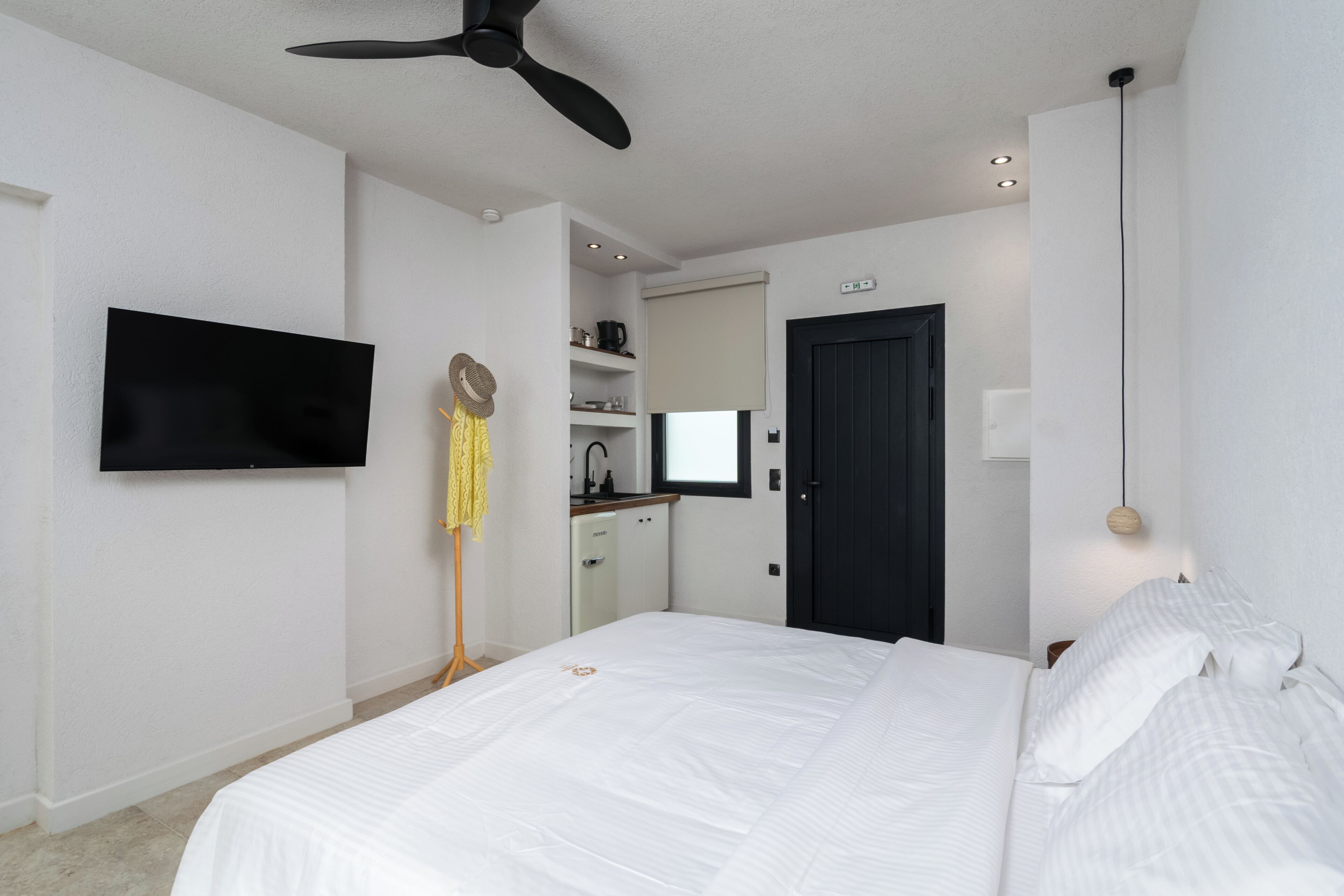 A bedroom with a bed, a ceiling fan, a TV, a wardrobe, and a door.