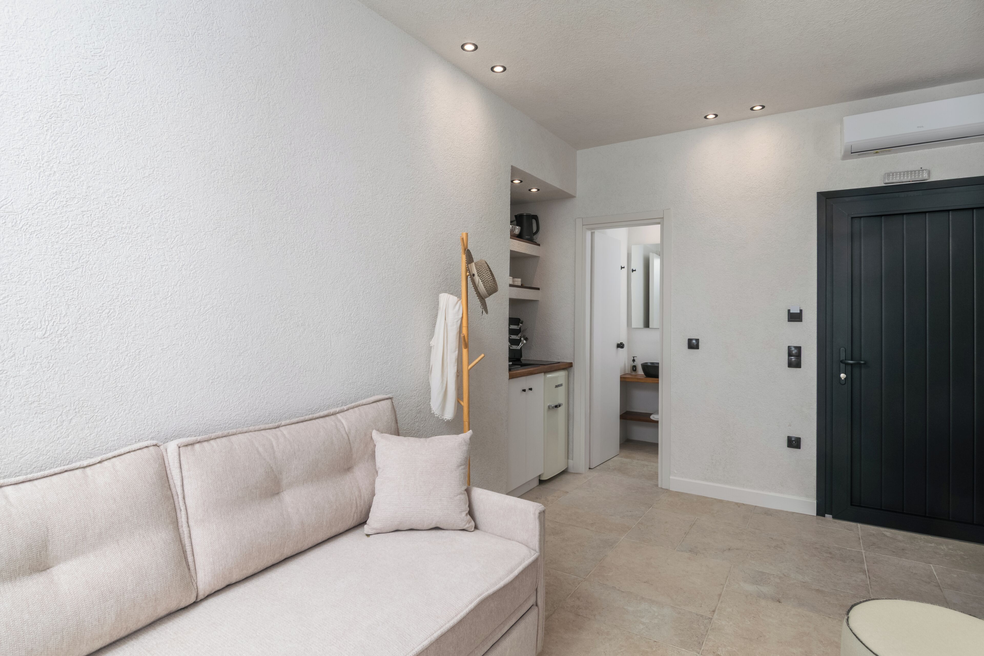 A modern living room with a sofa, a small table, and a door leading to a kitchen area.