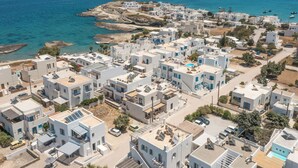 Una zona residencial costera con edificios blancos modernos, mar azul claro y terreno rocoso al fondo.