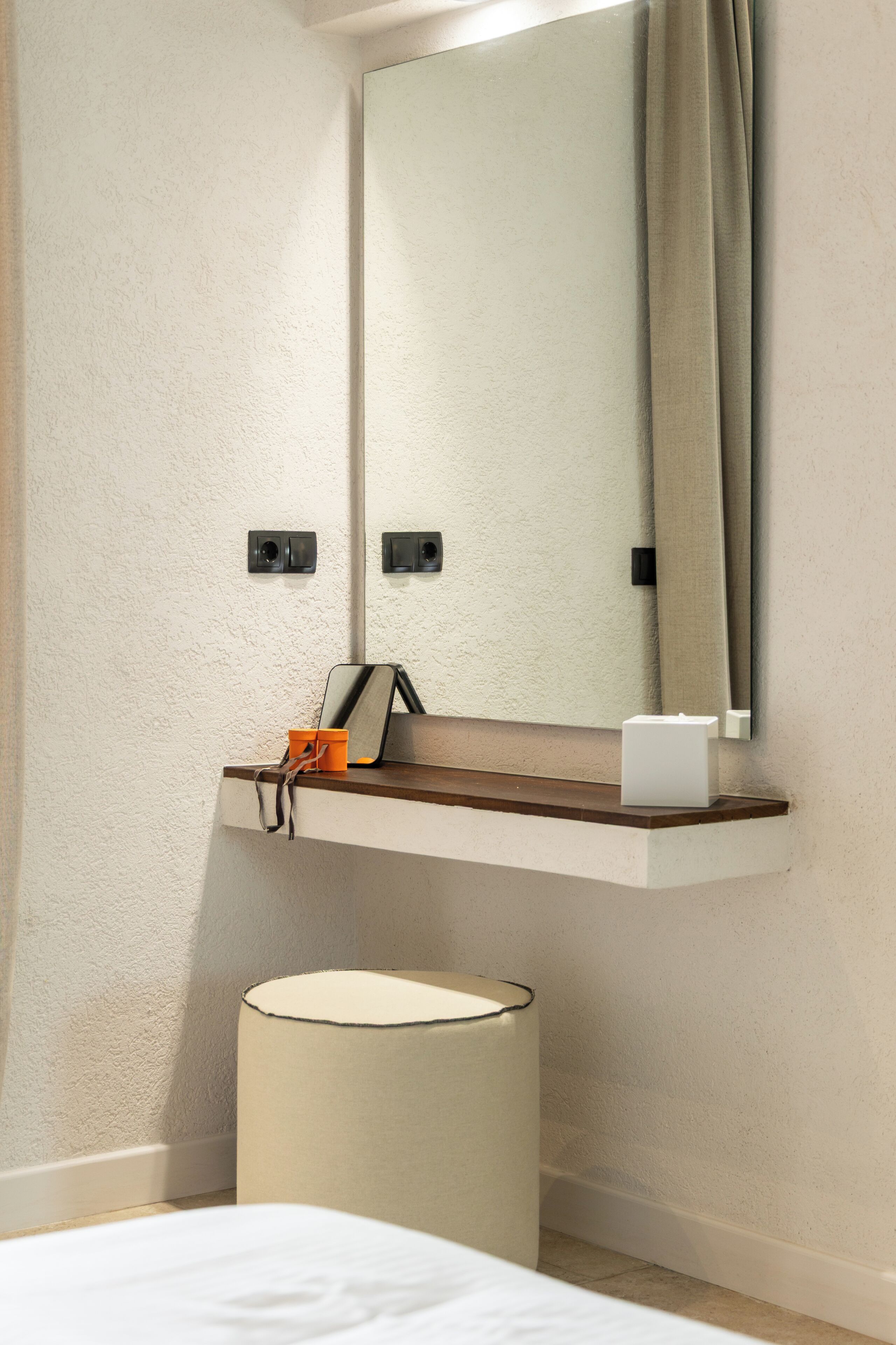 A bathroom with a mirror, a towel rack, a small shelf with a cup and a box, and a cylindrical container.
