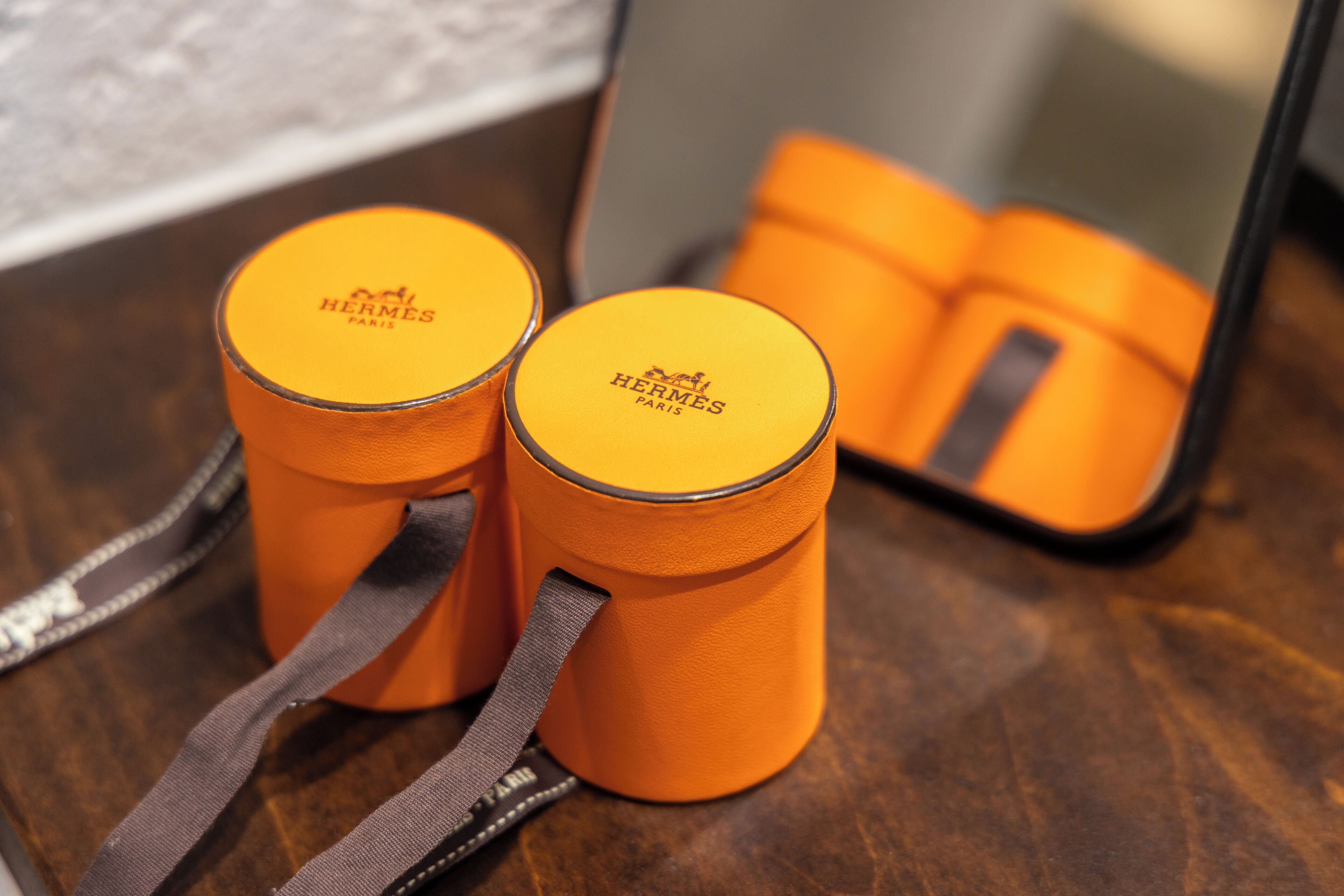 Two orange Hermes perfume containers with straps on a wooden surface.