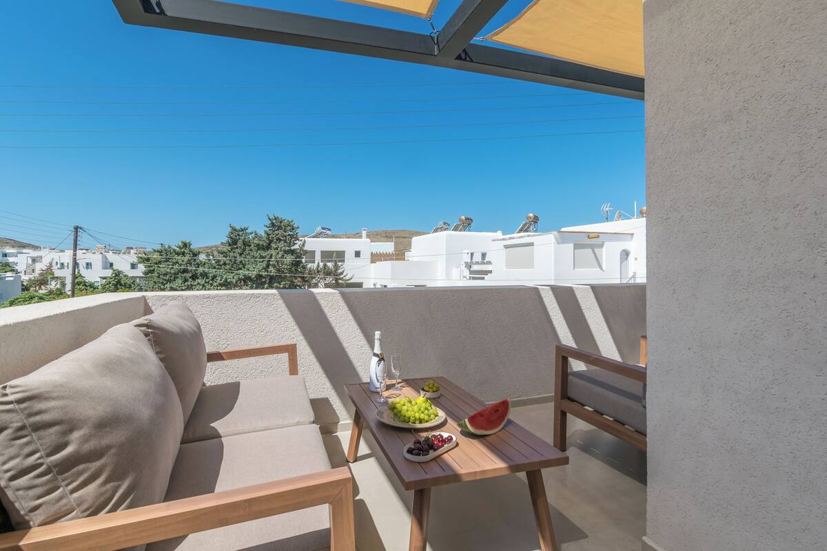 A balcony with a sofa, a table with fruit and a bottle, and a view of white buildings.