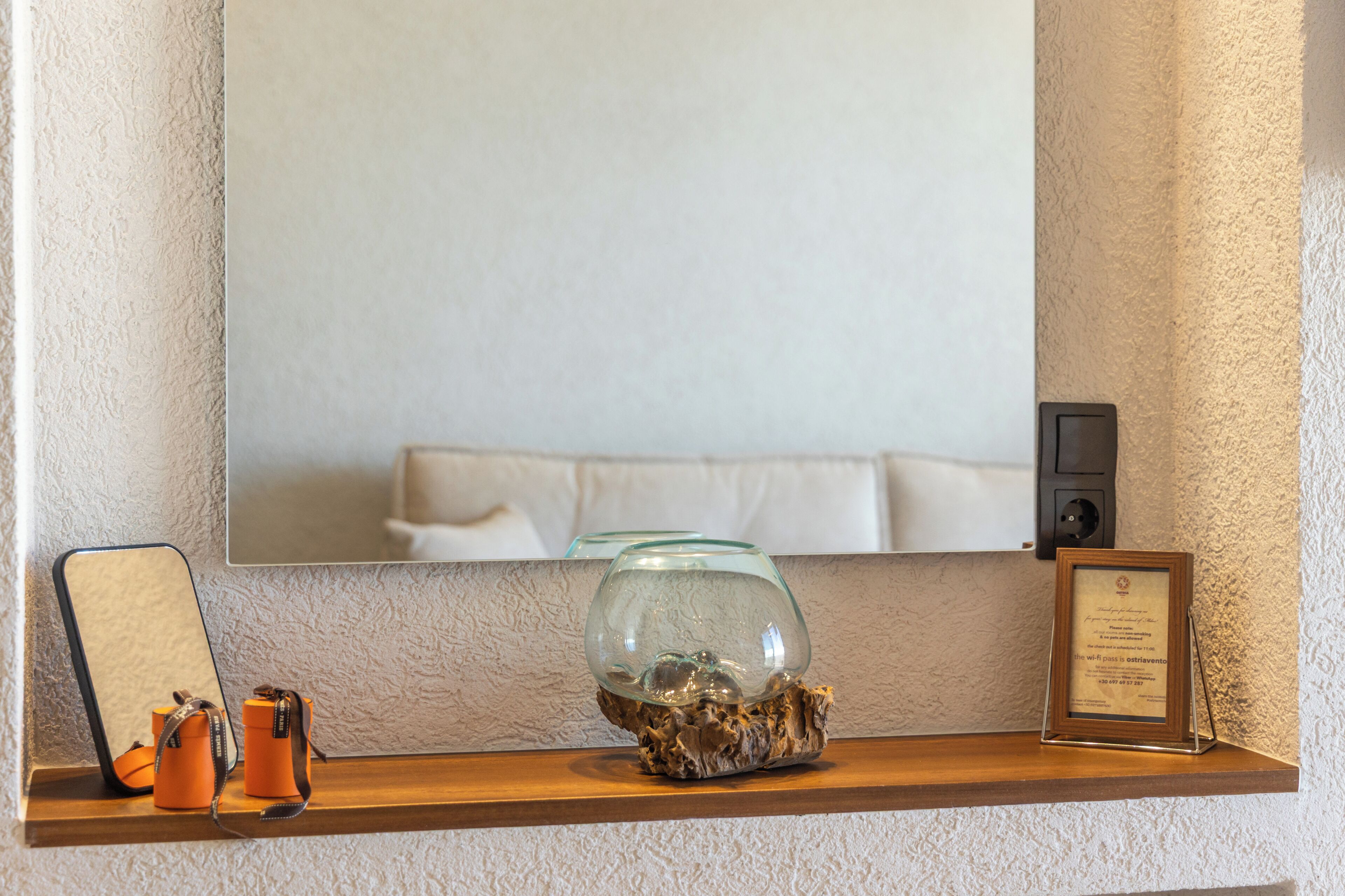 A mirror, a framed certificate, a glass bowl on a wooden shelf, and a camera on a shelf.