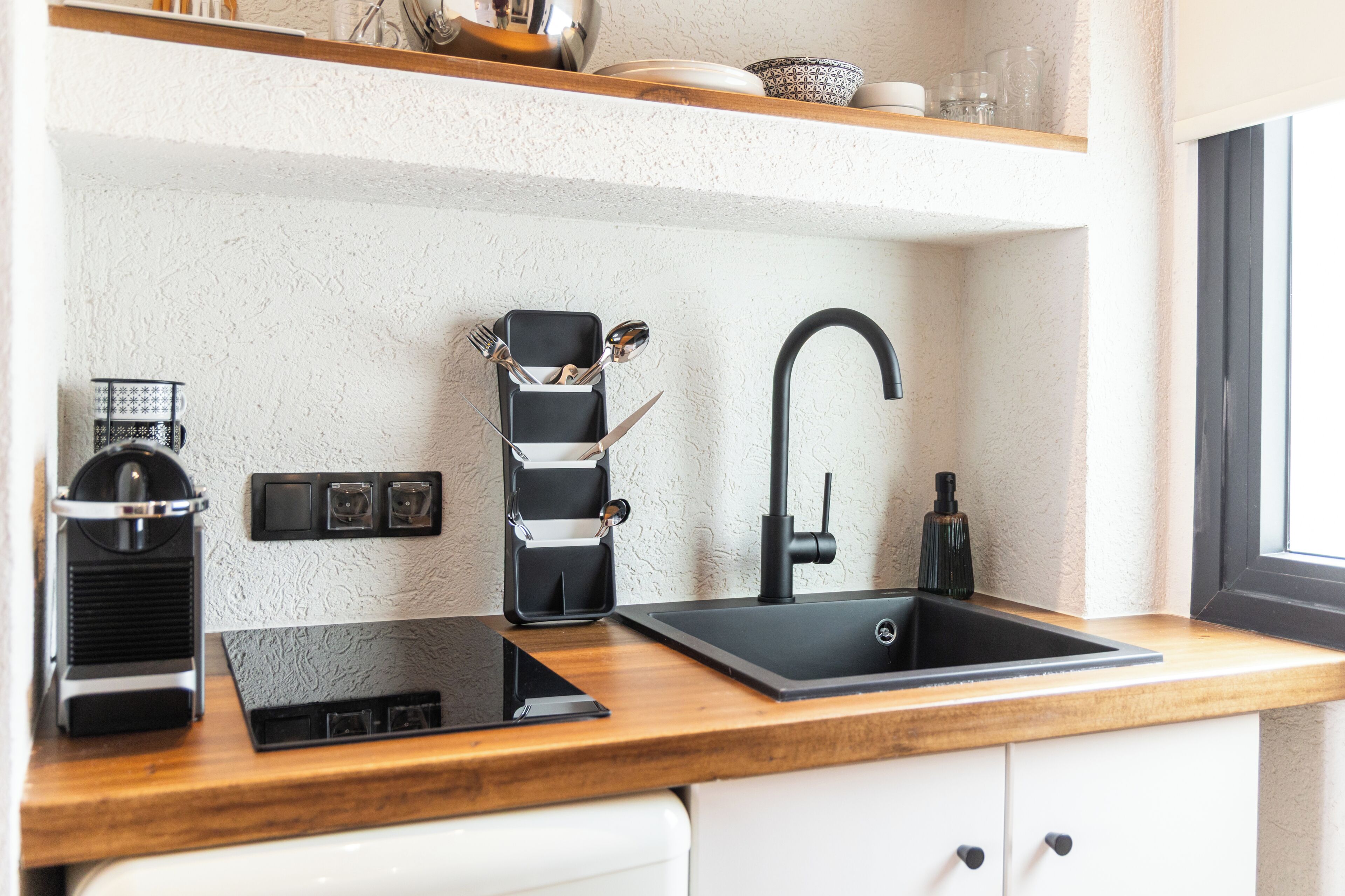 Een moderne keuken met een zwarte spoelbak, een koffieapparaat en een ingebouwd oplaadstation.