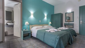 A hotel room with teal walls, a bed with white linens, two bedside tables with lamps, a large mirror, and a bathroom visible through an open door. - Armonia Apartments (Chania)