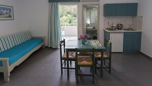 A compact living space with a sofa, dining table, chairs, a kitchen area, and a balcony with curtains. - Armonia Apartments (Chania)