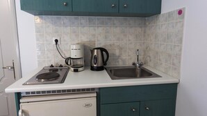 A compact kitchenette with a stove, coffee maker, kettle, and sink. - Armonia Apartments (Chania)