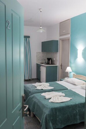 Une chambre d’hôtel avec deux lits, une kitchenette, un rideau de douche et une porte portant un numéro.