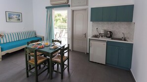 A compact kitchen with teal cabinets, a dining table with chairs, and a kitchenette. - Armonia Apartments (Chania)