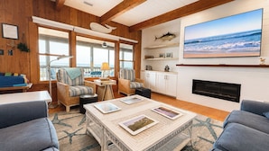 A cozy living room with a fireplace, comfortable seating, and a large TV mounted on the wall. - Captain's R&R - 5 BR Oceanfront Home w/Private Pool & Hot Tub - Dogs Allowed (Southern Shores)
