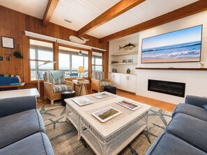 A cozy living room with a fireplace, comfortable seating, and a large TV mounted on the wall. - Captain's R&R - 5 BR Oceanfront Home w/Private Pool & Hot Tub - Dogs Allowed (Southern Shores)