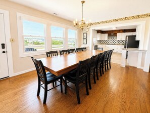 A spacious dining room with a large wooden table and chairs, a chandelier, and a view of the outside through large windows. - Captain's R&R - 5 BR Oceanfront Home w/Private Pool & Hot Tub - Dogs Allowed (Southern Shores)