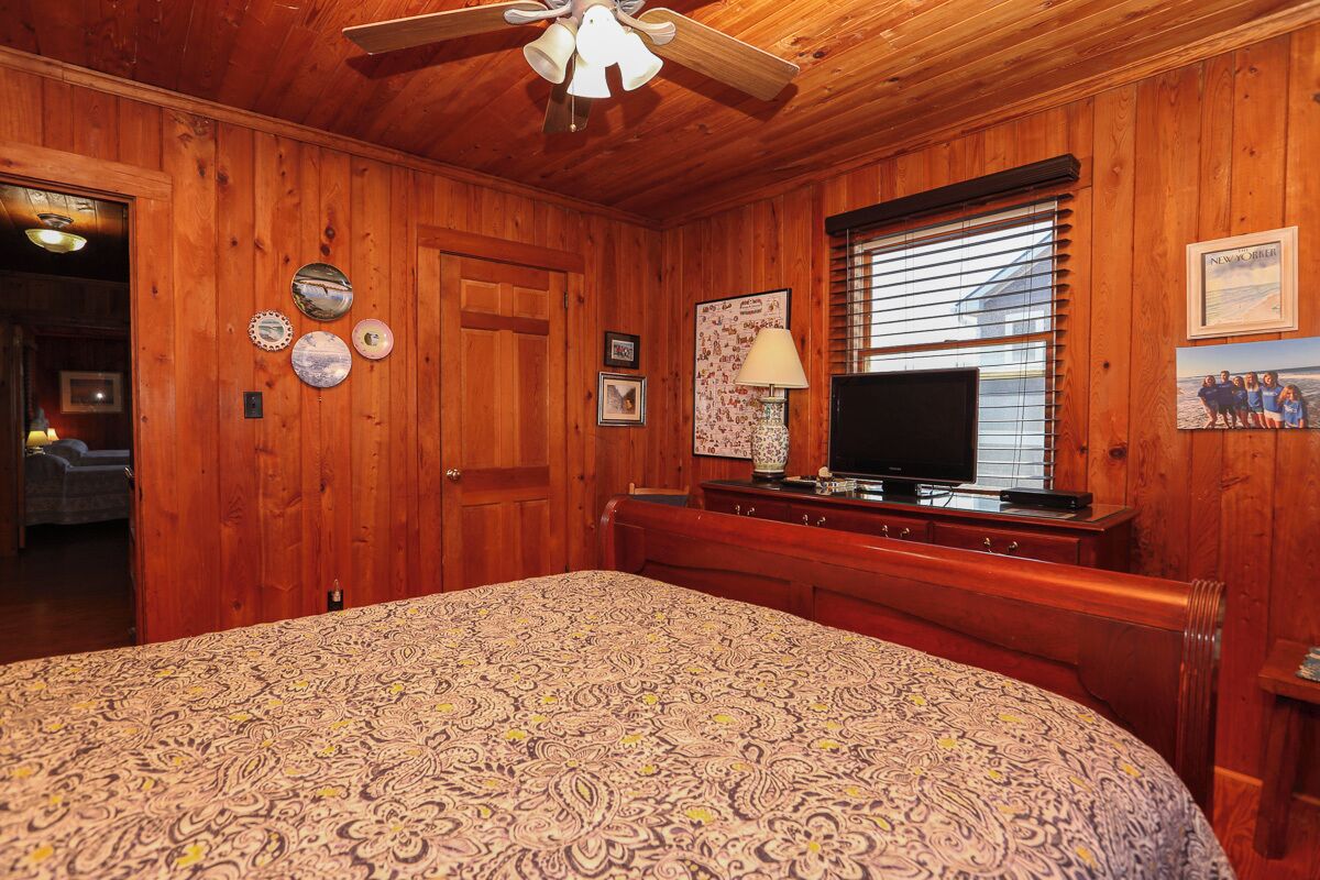 A wooden-paneled room with a bed, a television, and a window with blinds.