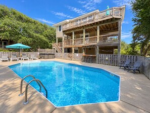 A swimming pool with a wooden deck, lounge chairs, and a multi-level building with balconies. - Saltwater Gospel - Oceanside 5 BR home w/Private Pool, Dogs Allowed (Duck)