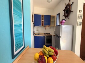 A kitchen with blue cabinets, a white refrigerator, and a fruit bowl on the counter. - Accommodation Just Steps Away From Cala Lupo (Stintino)