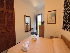 Un dormitorio con una cama, un armario de madera, un espejo, una silla, un escritorio y una ventana.