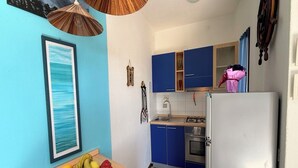 Eine Küche mit blauen Schränken, einem weißen Kühlschrank, einem Holztisch mit Obstkorb und einem gerahmten Bild an der Wand.