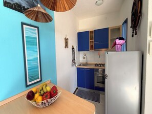 A kitchen with blue cabinets, a white refrigerator, a wooden table with a fruit basket, and a framed picture on the wall. - Accommodation Just Steps Away From Cala Lupo (Stintino)