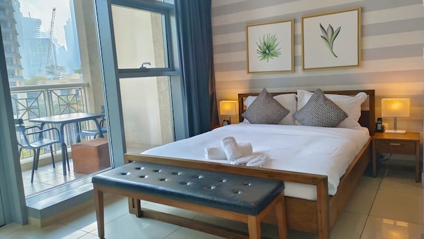 Ein Hotelzimmer mit einem großen Bett, zwei Nachttischlampen, einer Bank und Blick auf die Stadt durch ein großes Fenster.