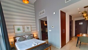 Ein modernes Hotelzimmer mit einem großen Bett, Nachttischen, einer Bank, einem Essbereich und einer Küche, die durch eine offene Tür sichtbar ist.