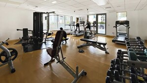 Ein Fitnessstudio mit verschiedenen Trainingsgeräten, großen Fenstern und einer aufgeräumten, übersichtlichen Gestaltung.