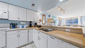 A modern kitchen with white cabinets, a double sink, and a built-in dishwasher. - Whaler 3C (Gulf Shores)