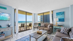 A living room with a sofa, coffee table, and a television on a wall. - Whaler 3C (Gulf Shores)