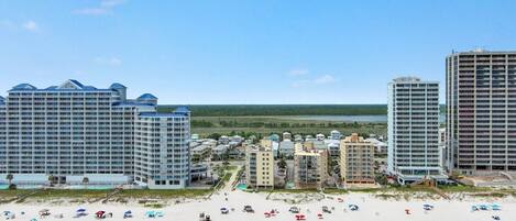 A beachfront hotel with multiple high-rise buildings, a sandy beach with umbrellas, and a view of the ocean.