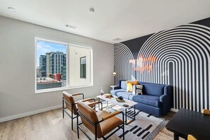 Ein modernes Wohnzimmer mit einer Couch, einem Couchtisch, Sesseln und Blick auf Gebäude durch ein großes Fenster.