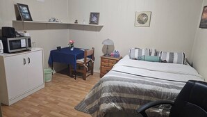 A small, tidy room with a bed, a desk, a chair, a microwave, and a shelf with decorative items. - Room-vermaurel Sweet Lodge (Bathurst)