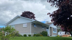 A two-story house with a front porch, a small garden, and a wooden deck. - Room-vermaurel Sweet Lodge (Bathurst)