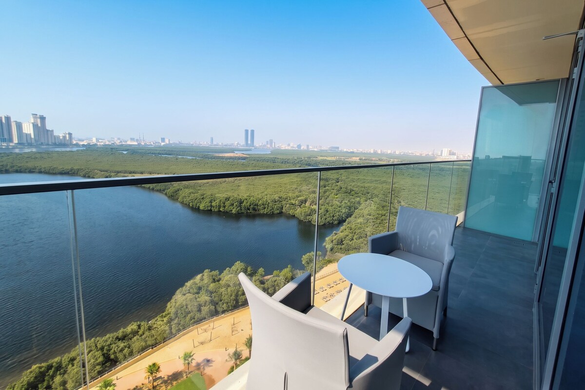 A modern balcony with a glass railing overlooking a river and cityscape.